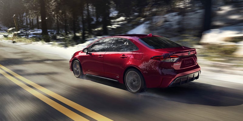 2027 Toyota Corolla Hybrid AWD driving smoothly along a snow-lined mountain road